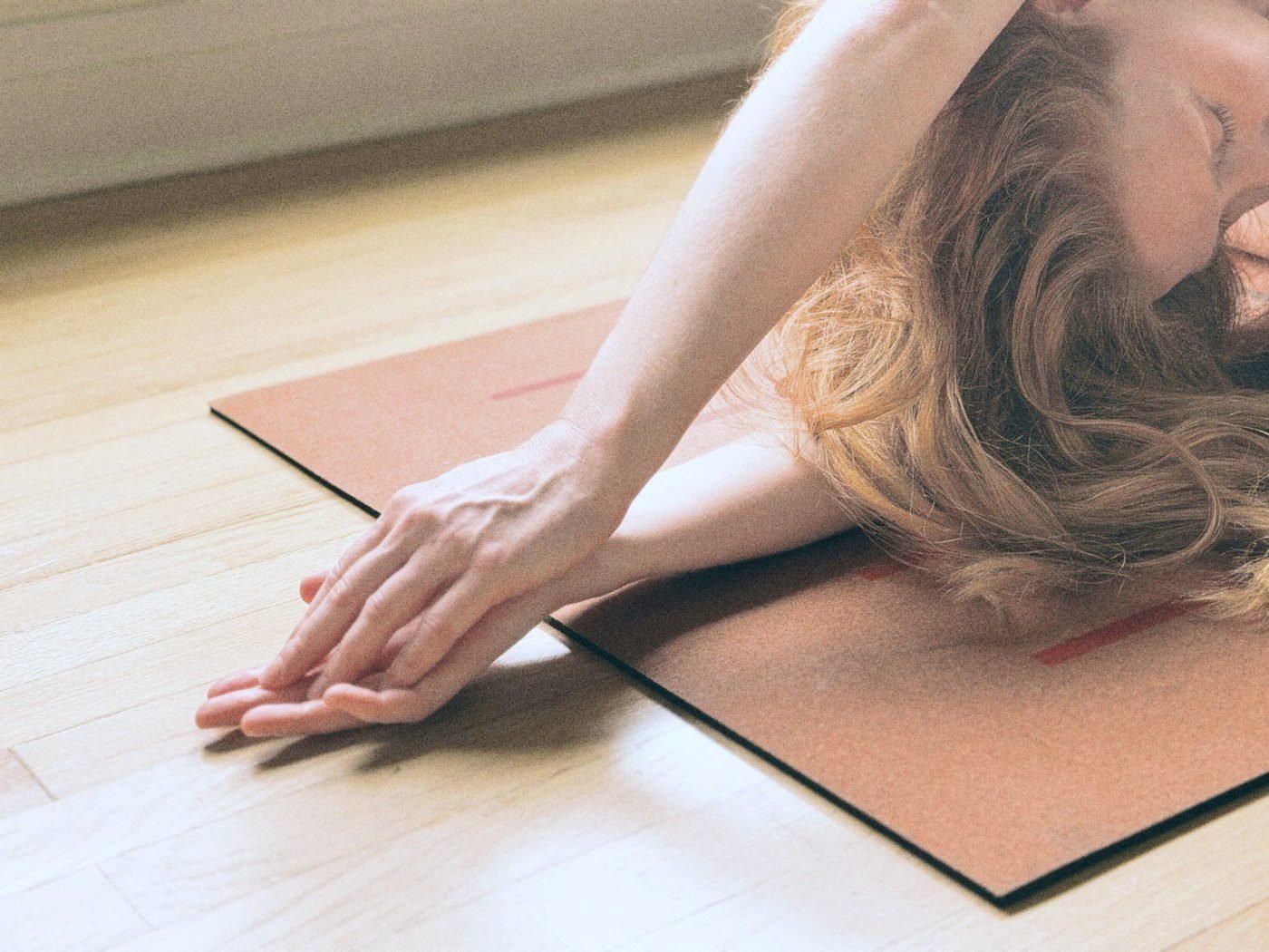 A relaxed hand resting on a cork mat, hair spread across the floor in soft light