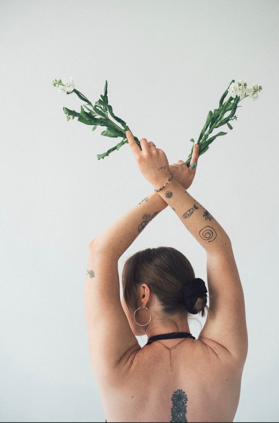 A yoga student seen from behind, arms crossed overhead holding white flowers