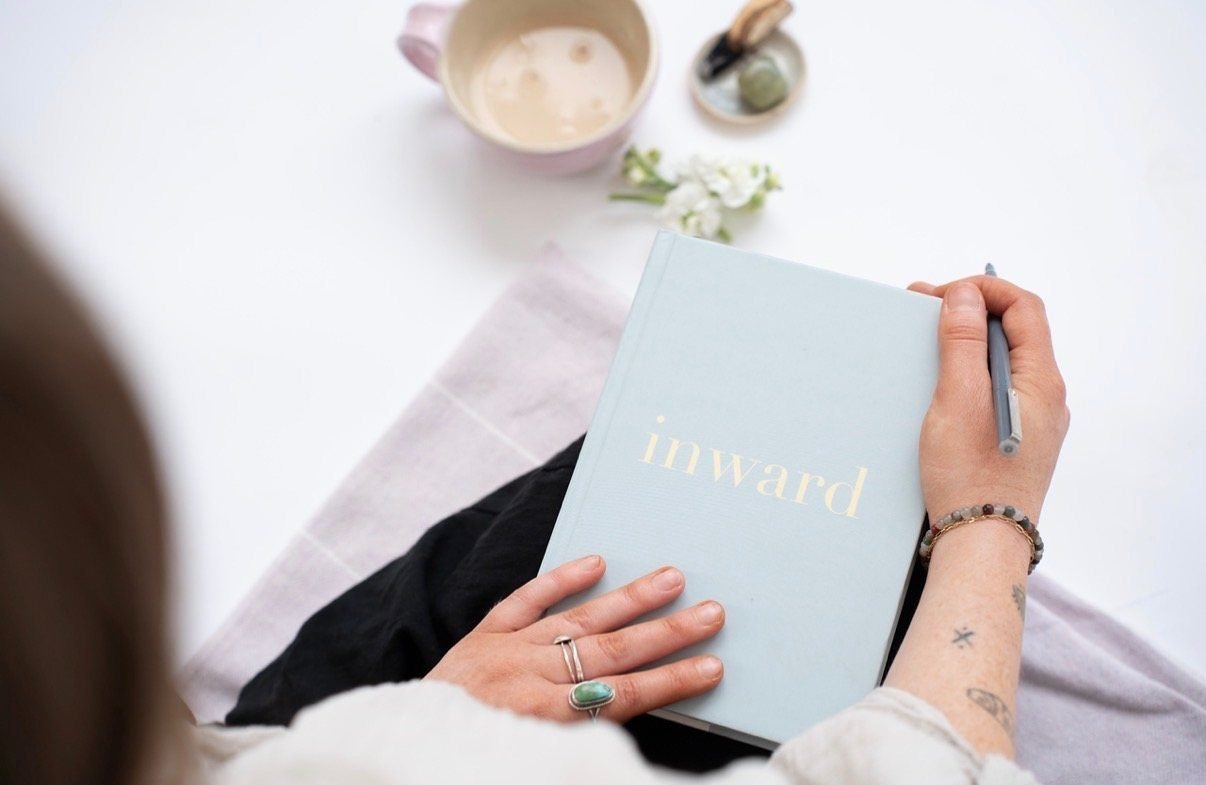 Hands resting on the Inward manual, pen in hand, tea and flowers nearby