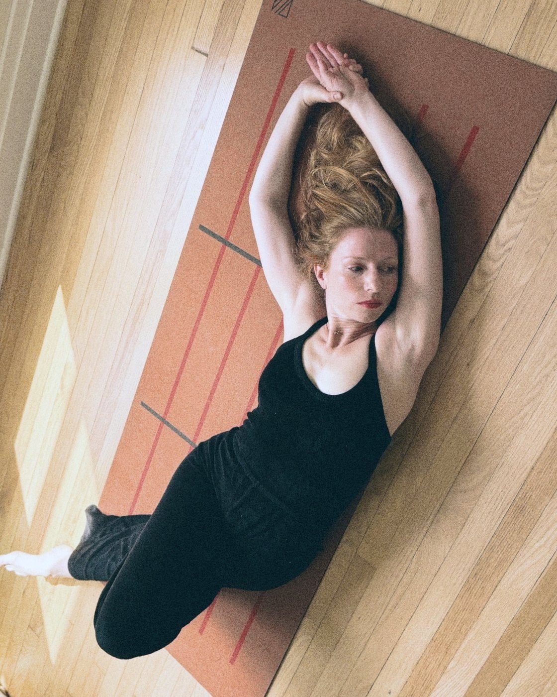 Kathryn lying on a cork mat in a reclined mermaid shape, arms overhead